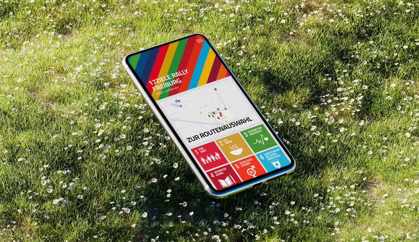 Mockup mit Smartphone auf Wiese, Screen zeigt Vorschau der 17 Ziele App der Stadt Freiburg