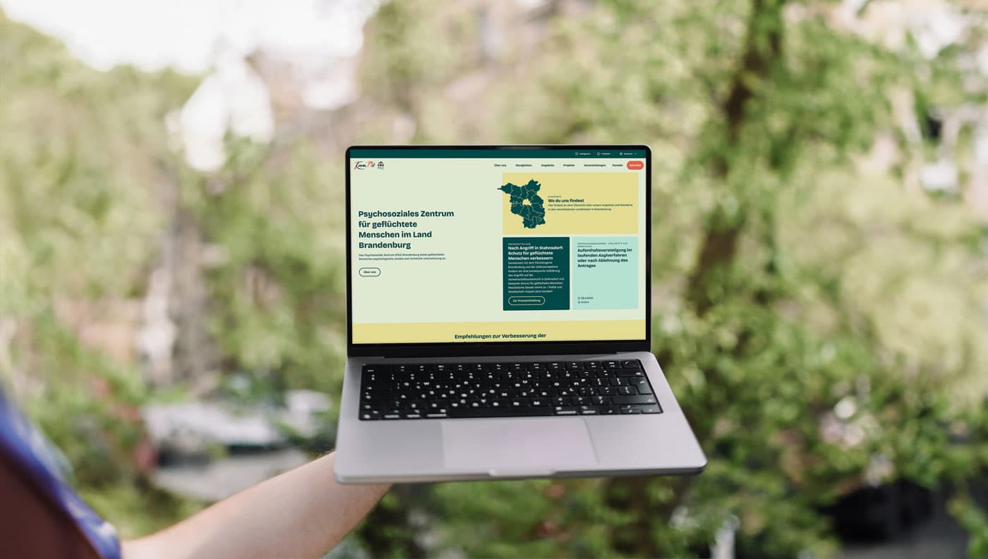 Laptop mit der neuen KommMit Webseite draußen vor grünem Hintergrund